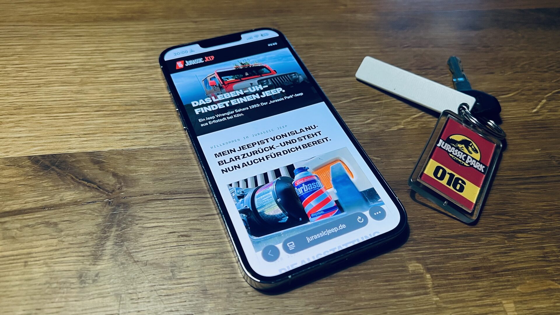 Die Homepage des Jurassic Jeep auf einem Apple iPhone 13 Pro Max, daneben ein Autoschlüssel eines Jeep Wrangler mit „Jurassic Park“-Schlüsselanhänger